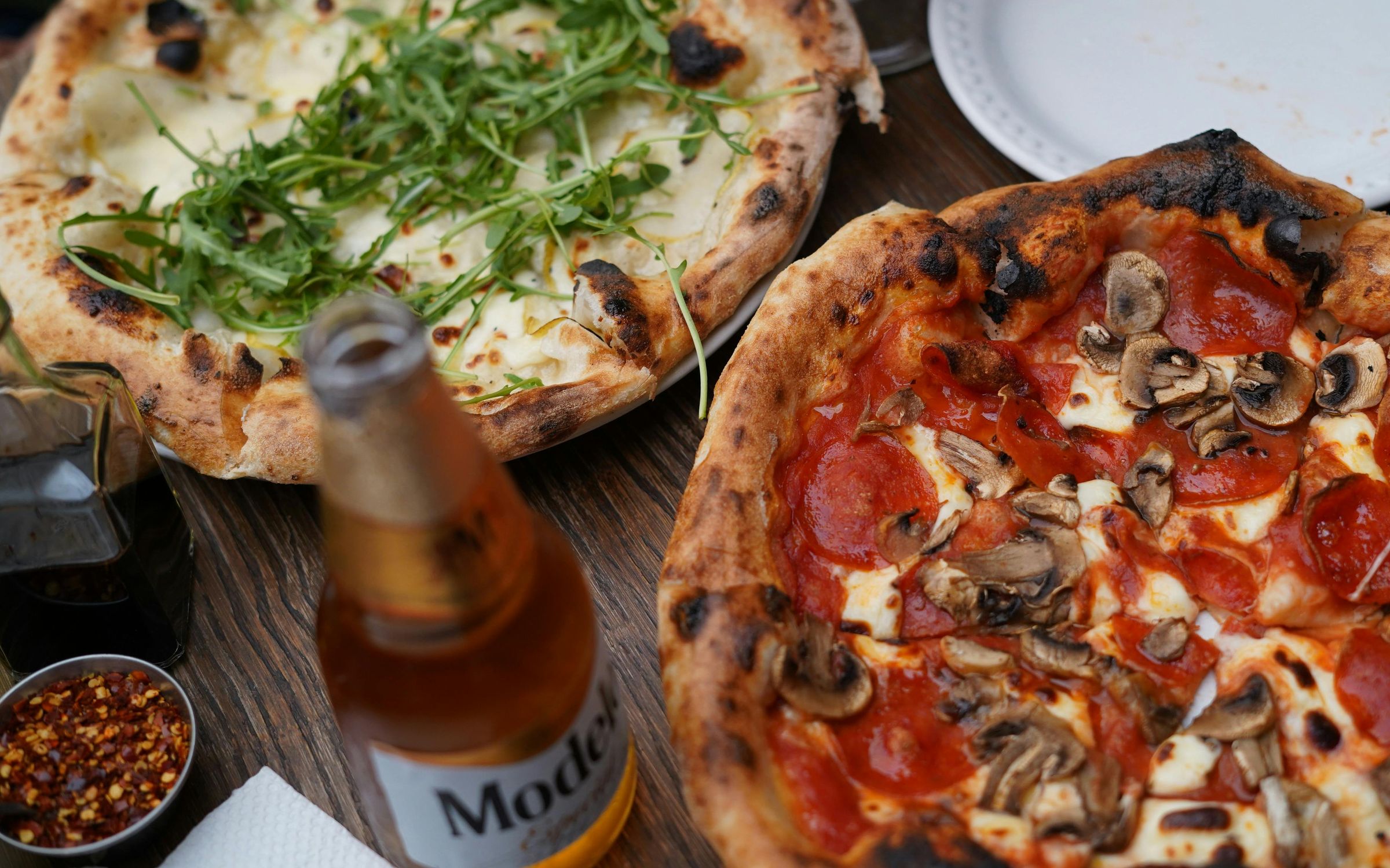Wood-fired pizzas and a cold beer on a timber table
