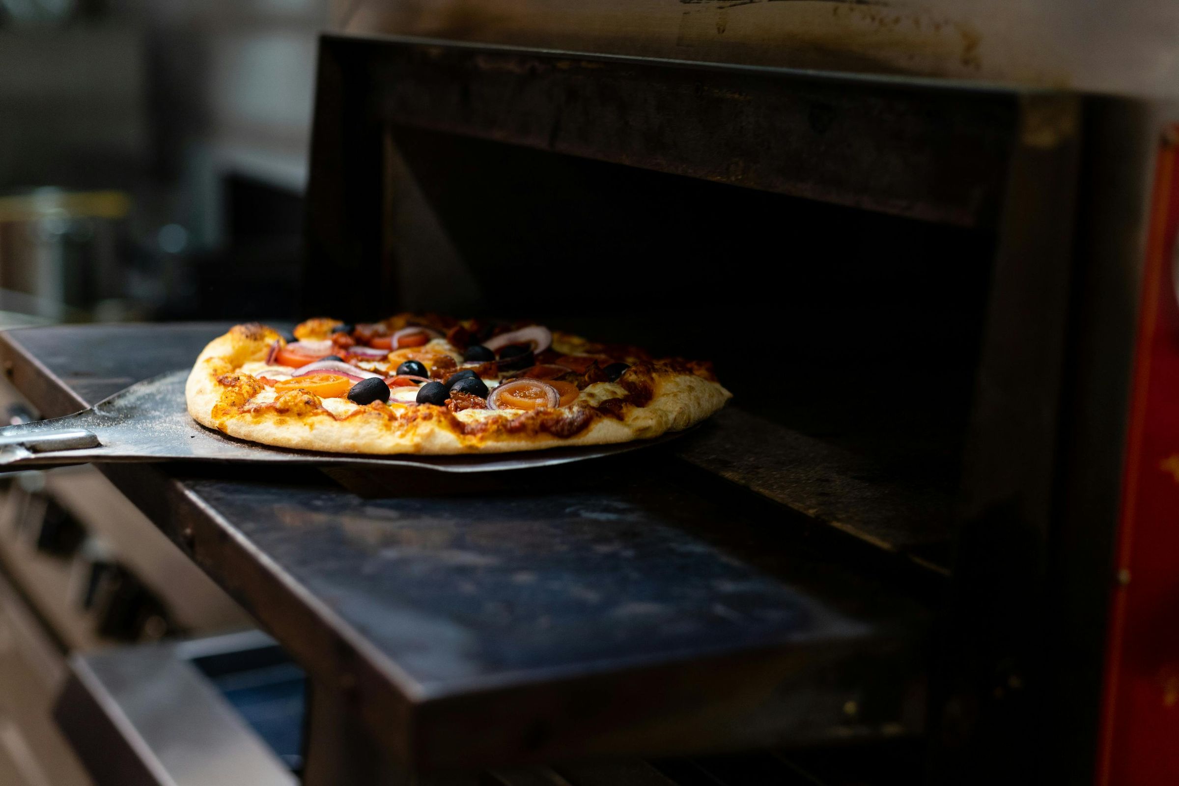 A pizza coming out of the brick oven